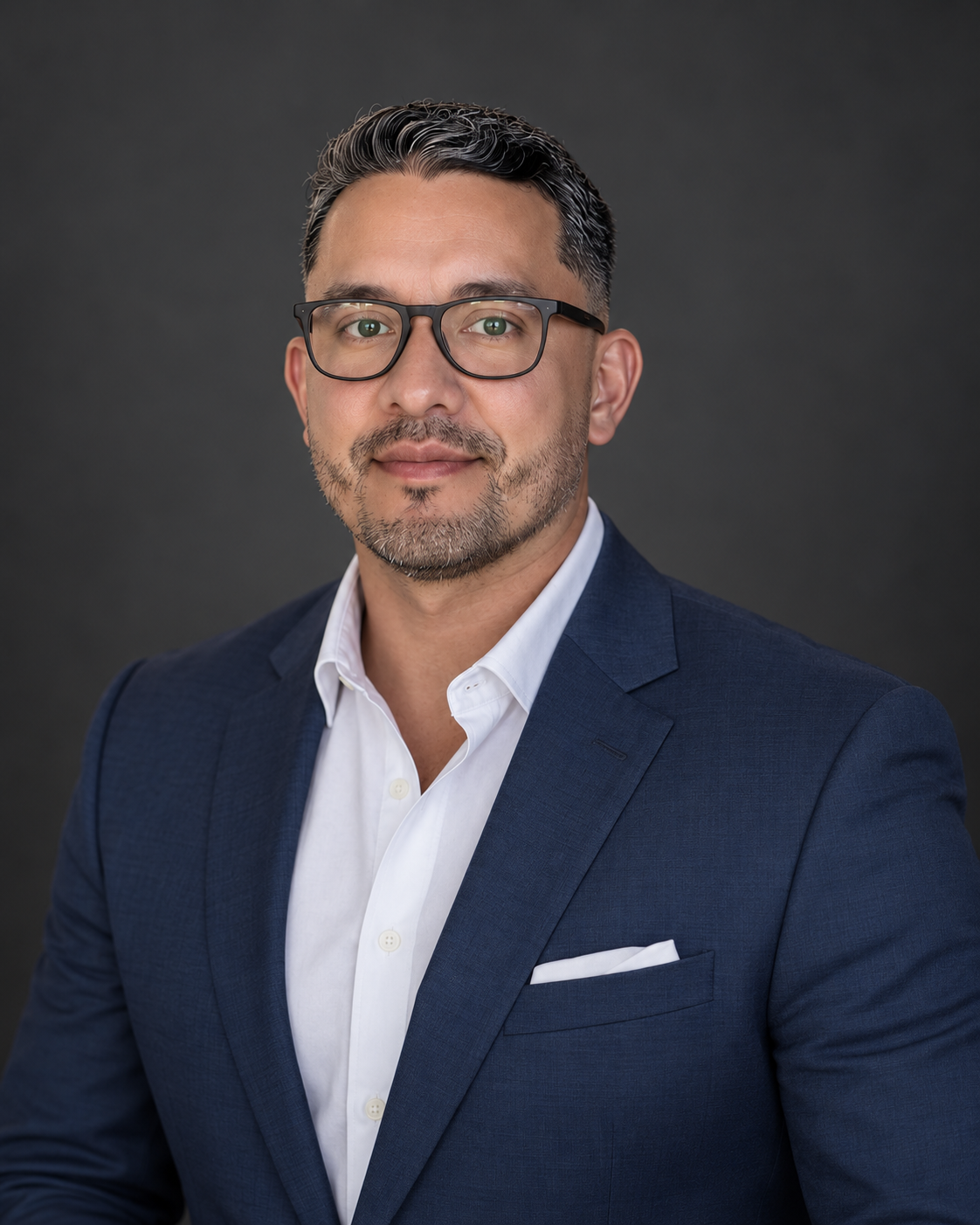 Daniel E. Torres in a navy suit, glasses and an open-collar white shirt